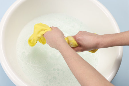 Woman washing baby clothes in basin on light blue background, closeupの写真素材
