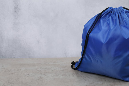 Blue drawstring bag on grey textured table. Space for text