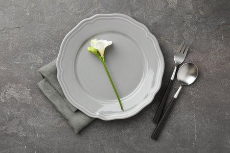 Stylish setting with cutlery, napkin, flower and plate on grey textured table, flat layの写真素材