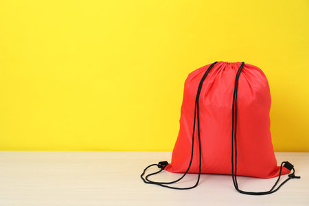 Red drawstring bag on white wooden table against yellow background. Space for textの写真素材