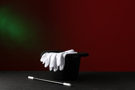 Magician's hat, wand and gloves on black wooden table against dark backgroundの写真素材