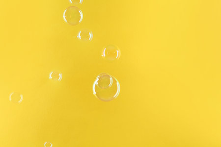 Beautiful transparent soap bubbles on yellow background, space for textの写真素材