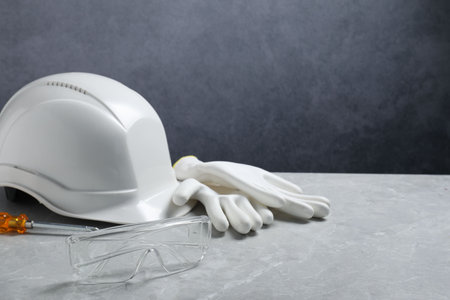 Hard hat, protective gloves, goggles and screwdriver on gray surface. Space for text