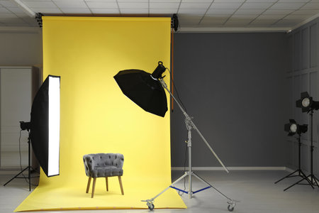 Yellow photo background, armchair and professional lighting equipment in modern studio