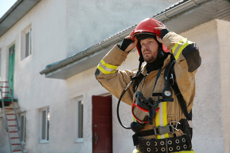 Firefighter in uniform with helmet near station outdoors, space for text