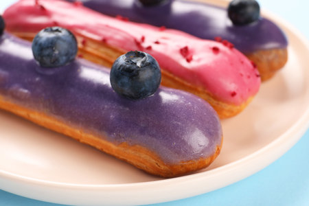 Delicious eclairs covered with glaze on light blue background, closeup