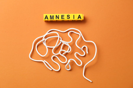 Word Amnesia and brain made of wires on orange background, flat lay