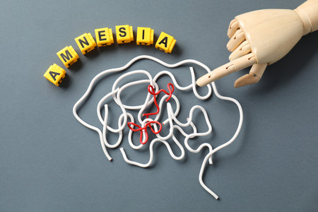 Word Amnesia, brain made of wires and mannequin hand on gray background, flat lay