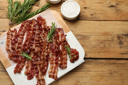 Slices of tasty fried bacon, rosemary and salt on wooden table, top view, space for textの写真素材