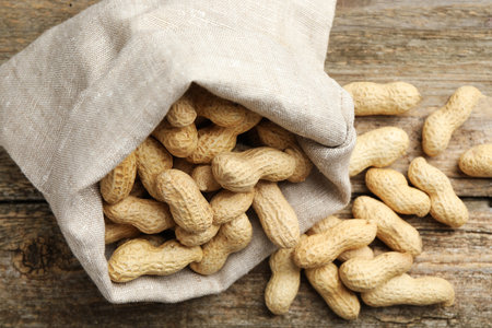 Fresh unpeeled peanuts in sack on wooden table, above view