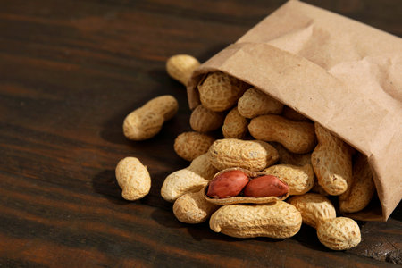 Paper bag with fresh unpeeled peanuts on wooden table, closeup. Space for text