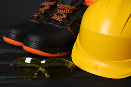 Pair of working boots, hard hat and goggles on black wooden surface, closeupの写真素材