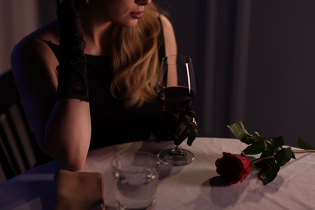 Elegant young woman with glass of wine at table indoors in evening, closeupの写真素材
