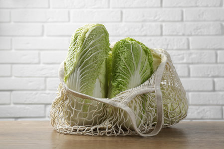 Fresh Chinese cabbages in string bag on wooden table near white brick wallの写真素材