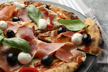 Tasty pizza with cured ham, olives, mozzarella cheese, sun-dried tomato and basil on table, closeupの写真素材