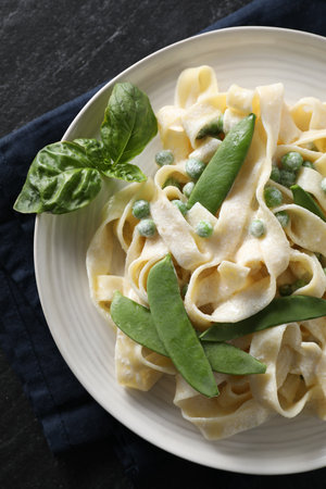 Delicious pasta with green peas and creamy sauce on black table, top viewの写真素材