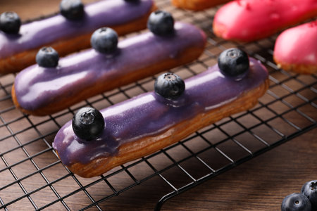 Cooling rack with different tasty glazed eclairs on wooden table, closeupの写真素材
