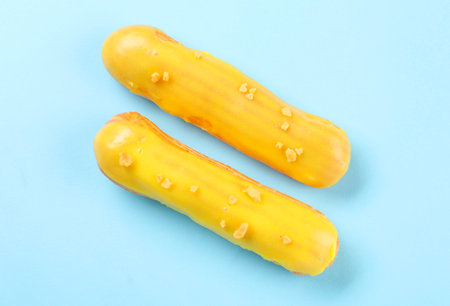 Delicious eclairs covered with glaze on light blue background, top view