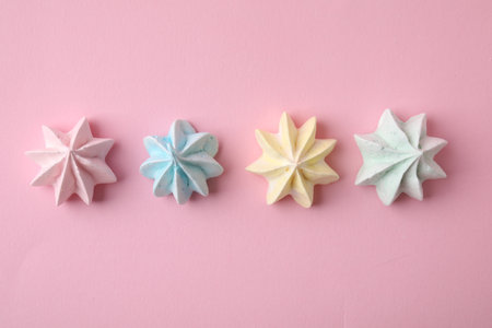 Many tasty meringue cookies on pink background, flat lay