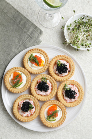 Delicious canapes with salmon, caviar, microgreens and glass of water on beige textured table, flat layの写真素材