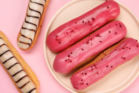 Delicious eclairs covered with glaze on pink background, flat lay