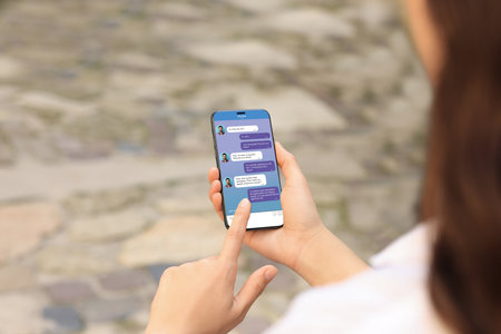 Woman texting via mobile phone outdoors, closeup. Device screen with messagesの写真素材
