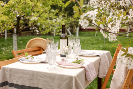 Stylish table setting with beautiful spring flowers, wine, plates and glasses in gardenの写真素材