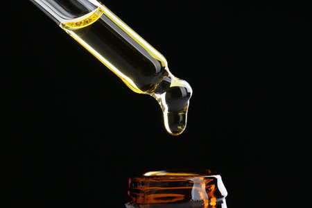 Dripping tincture from pipette into bottle on black background, closeup