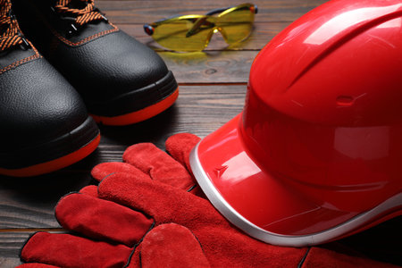 Hard hat, pair of working boots, protective gloves and goggles on wooden background, closeupの写真素材