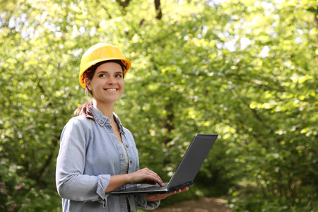 Forester with laptop examining plants in forest, space for text