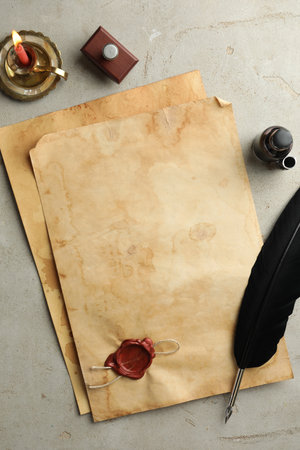 Sheet of old parchment paper with wax stamp, black feather, inkwell and candle on grey table, flat layの写真素材