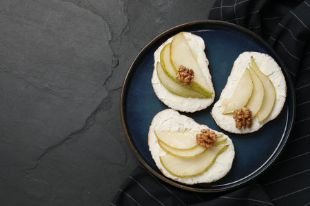 Delicious bruschettas with ricotta cheese, pears and walnuts on dark textured table, top view. Space for textの写真素材