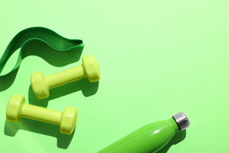 Dumbbells, fitness elastic band and water bottle on light green background, flat lay. Space for textの写真素材