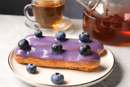 Tasty glazed eclair with blueberries on gray marble table, closeup