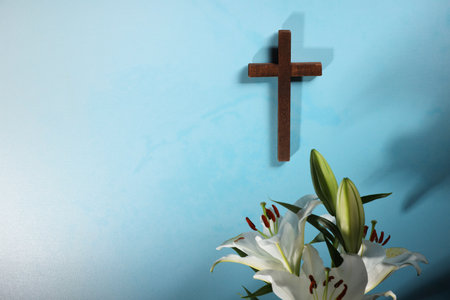 Wooden cross and lily flowers on light blue background, space for text. Religion of Christianityの写真素材
