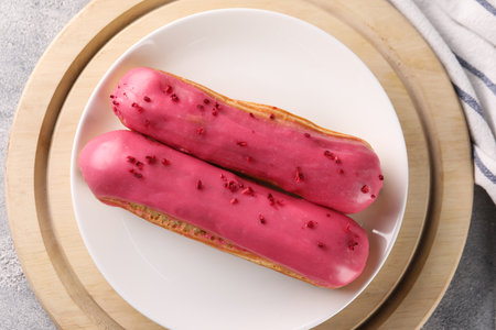 Plate with tasty glazed eclairs on gray table, top view