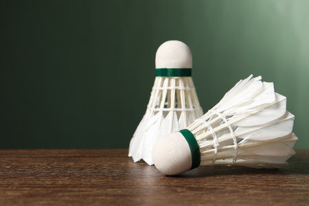 Feather badminton shuttlecocks on wooden table against green background, closeup. Space for text