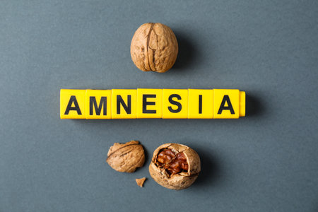Word Amnesia made of yellow cubes and walnuts on gray background, flat lay