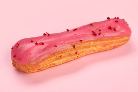 Delicious eclair covered with glaze on pink background