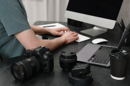 Camera on dark table, closeup. Photographer working with computer indoors, selective focusの写真素材