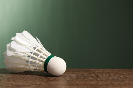 Feather badminton shuttlecock on wooden table against green background, closeup. Space for textの写真素材