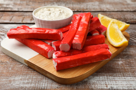 Tasty crab sticks, sauce and lemon wedges on wooden table, closeupの写真素材