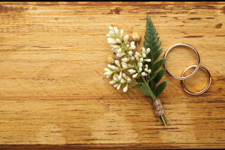 Small stylish boutonniere and rings on wooden table, flat lay. Space for text
