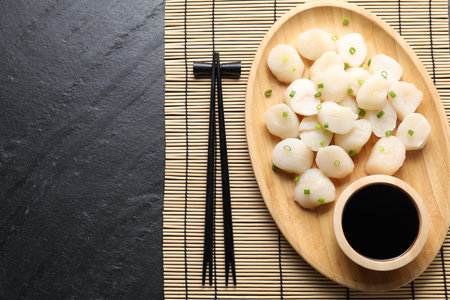 Raw scallops with green onion, soy sauce and chopsticks on dark textured table, top viewの写真素材