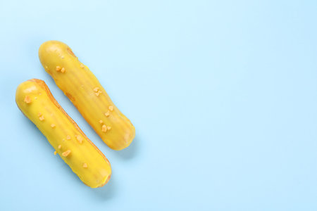 Delicious eclairs covered with glaze on light blue background, top view. Space for text