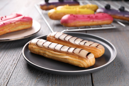 Different tasty glazed eclairs on wooden rustic table, closeup