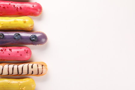Delicious eclairs covered with glaze on white background, top view