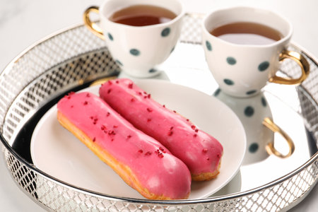 Tray with tasty glazed eclairs and tea on white table, closeupの写真素材