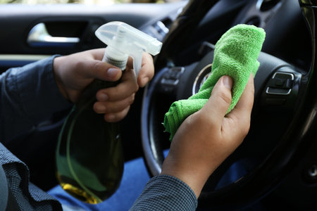Man steering cleaning wheel with rag and spray bottle in car, closeup
