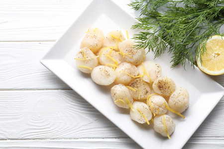 Raw scallops with milled pepper, lemon zest and dill on white wooden table, flat layの写真素材